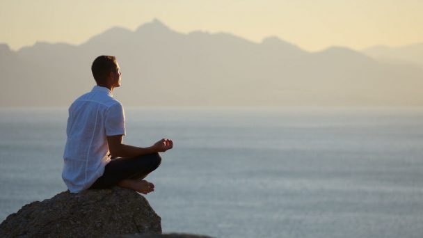 Guy sitting on a rock in the lotus position and looking at the setting sun